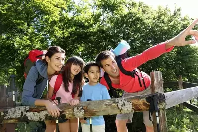 A happy family of four hiking in the woods with backpacks.
