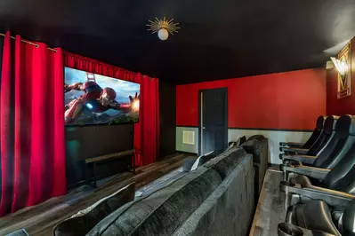 Cozy movie theater room with a comfortable couch and several neatly arranged chairs. Warm red walls create a welcoming ambiance. The room exudes a homely feel, perfect for enjoying a movie night with friends and family.