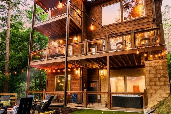 Luxury cabin with multiple decks with string lights, hot tub, and backyard with fire pit and mini golf