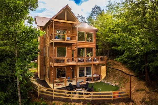 Luxury cabin with multiple decks with string lights, hot tub, and backyard with fire pit and mini golf