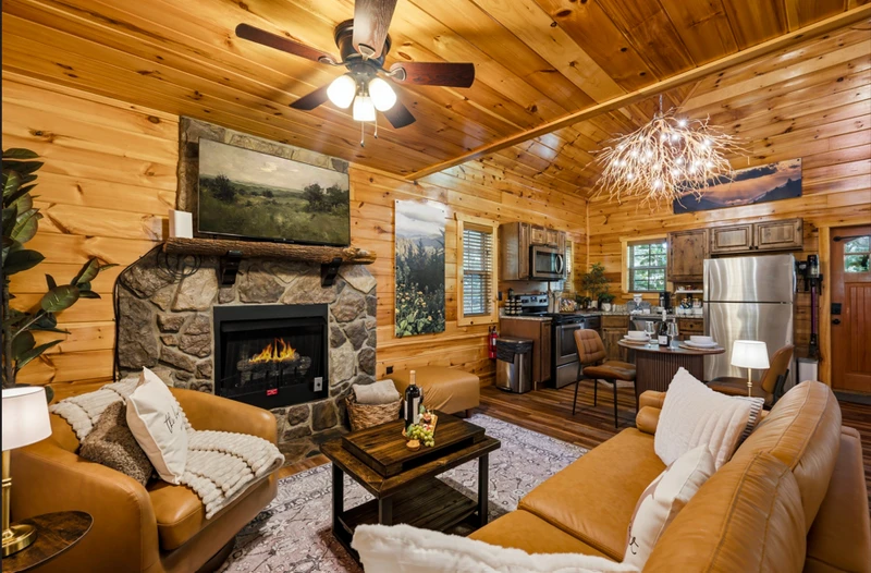 Inviting open‑concept living room with glowing fireplace, soft leather seating, and warm wood interiors — the perfect space to unwind after a day in the treetops.