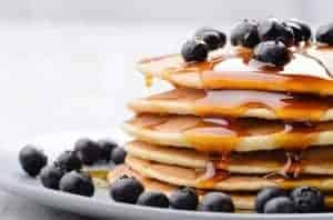 Blueberry pancakes with fresh blueberries and maple syrup on white plate