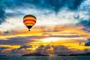 Hot air balloon flying over the sea into the sunset
