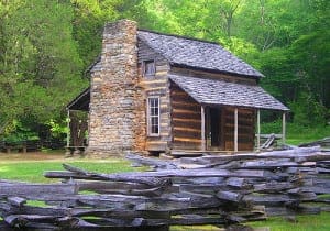 historic log cabin set back in woods with fence surrounding