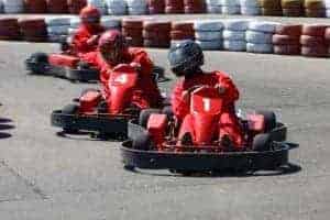 Three helmeted drivers dressed in red race red go karts
