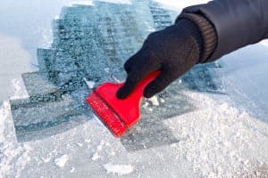 Hand wiping snow and frost off of a car windshield