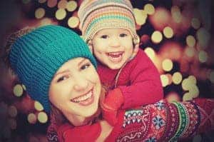 Mother and daughter laughing in winter clothes in front of holiday lights