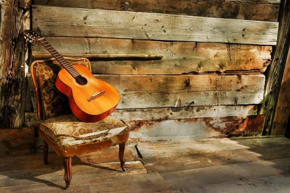 Brown acoustic guitar propped up on a chair in a rustic setting