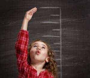 Girl measuring how tall she is against a black board