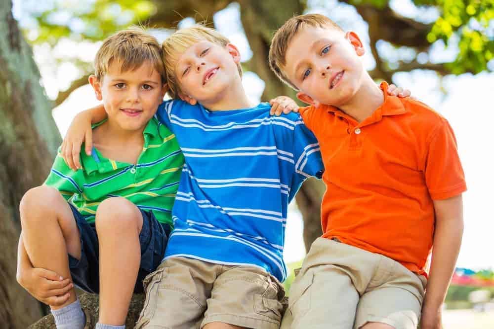 Three kids sitting outside together and smiling