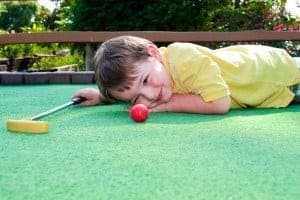 Kid laying down on the putting green playing mini golf