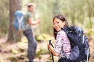 Happy couple with backpacks and poles hiking in the woods.