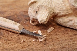 A bear carved out of wood with a small knife next to it.