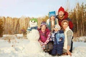 A happy family posing for a photo next to a snowman they built.