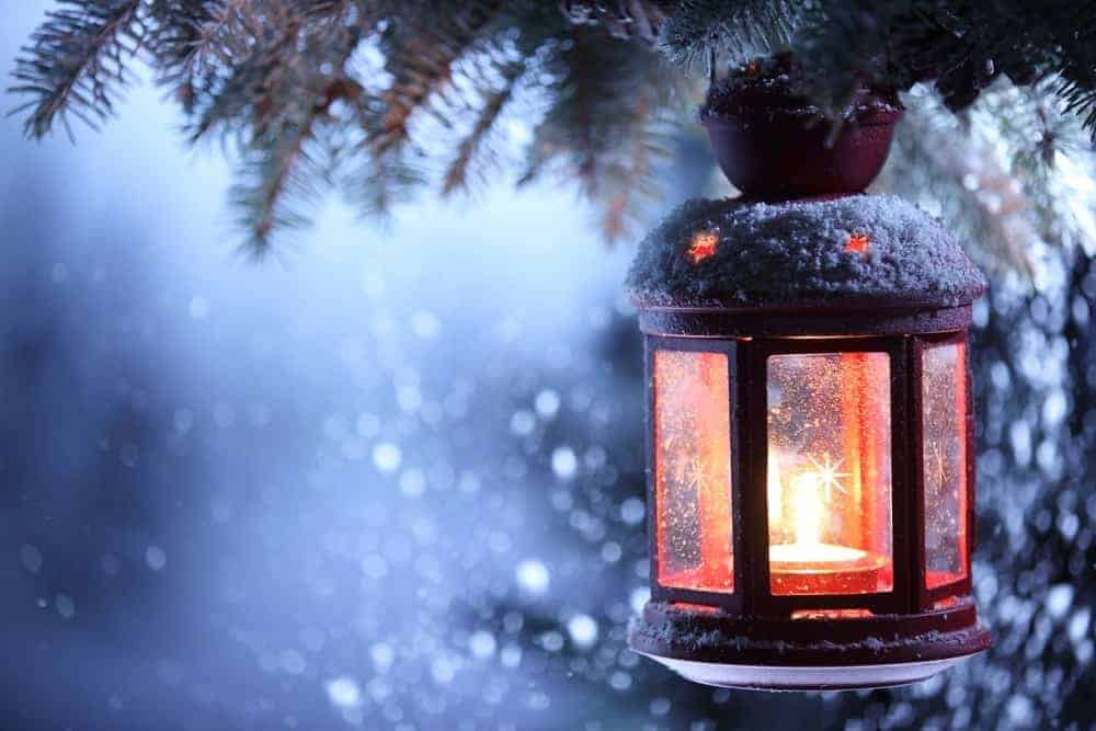 A snowy Christmas scene with a lantern hanging from a tree.