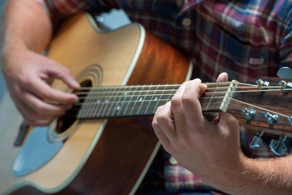 Closeup of a man playing country music on an acoustic guitar.