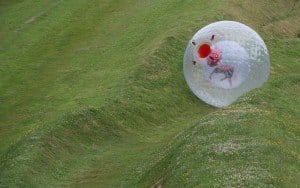 Photo of a man zorbing down a hill covered in grass.