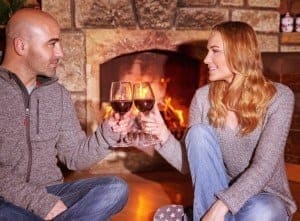 A couple sitting in front of their stone fireplace drinking wine.