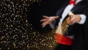 A magician pointing his wand at the camera as sparks fly out of it.