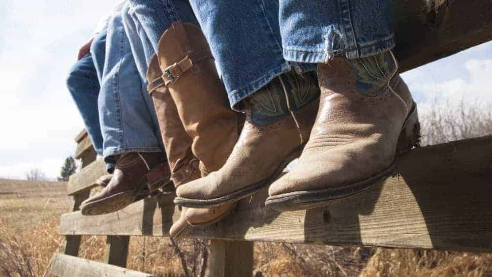 People wearing boots while sitting on a fence