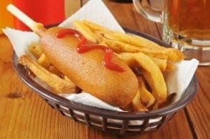 A big corn dog with ketchup and french fries.