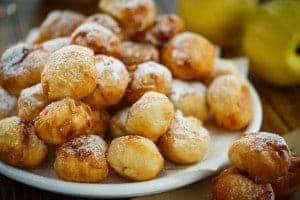 A plate of fried apple fritters with powdered sugar.