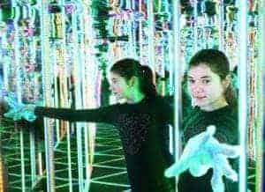 A girl wearing gloves making her way through a mirror maze.