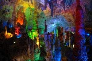 Stalactites and stalagmites covered in colorful lights in a cave.