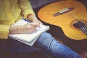 A woman writing music with a guitar next to her.