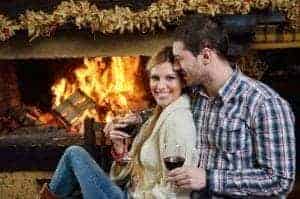 A romantic couple drinking wine beside their fireplace.