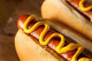 Hot dogs with yellow mustard on a wood table.