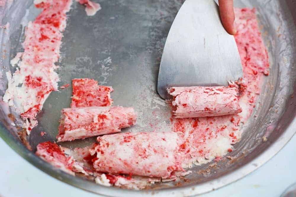 Rolled ice cream being scraped from a pan.