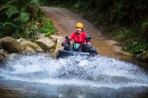 A college student riding an ATV through a river.