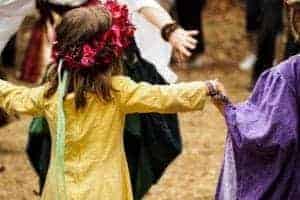 A little girl with flowers in her hair dancing around the maypole.