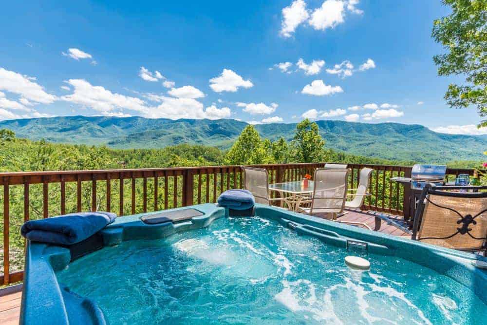 hot tub and tables on deck of cabin with mountain views