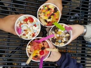 four hands holding four cups of frozen yogurt with toppings