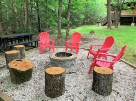 Spacious secluded backyard showing a fire pit with red deck chairs and lots of trees in a park like setting